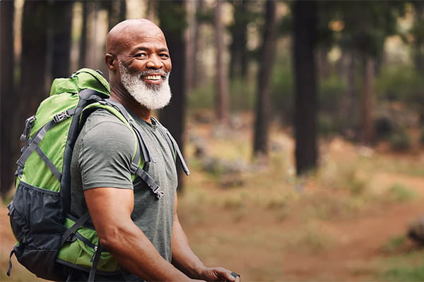 A fit man wearing a backpack is hiking through the woods.
