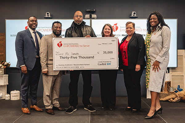 Ali Simeto, along with a group of judges and representatives, is holding a big check from the American Heart Association showing his 1st place win at the ETS Maryland Black Farmers Business Accelerator finale.