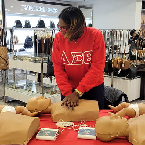 A Baltimore Delta Sigma Theta sorority member is practicing chest compressions on a CPR dummy inside a retail store.