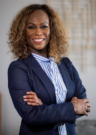 a professional photo of Pamela Garmon Johnson, a Black woman smiling and standing with arms crossed, wearing a navy blazer and blue and white striped blouse
