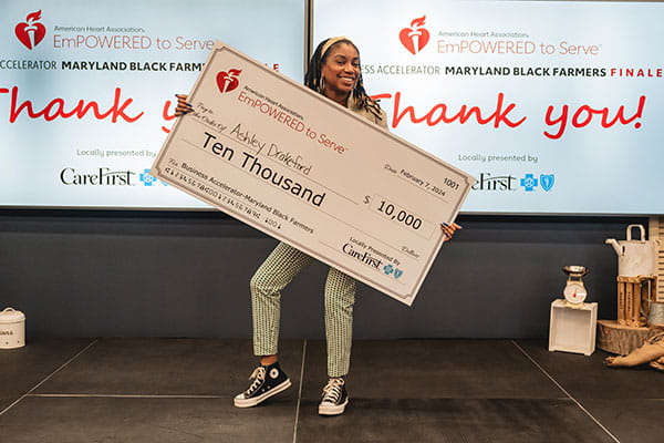 Ashley Drakeford is holding a big check from the American Heart Association showing her 3rd place win at the ETS Maryland Black Farmers Business Accelerator finale.