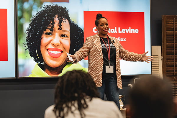 Crystal Levine with CodaBax is speaking to an audience in front of a large digital display.
