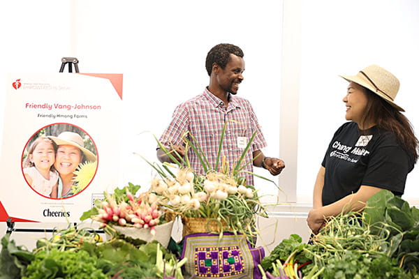 Friendly Vang-Johnson is talking with her staff member surrounded by fresh produce from Friendly Hmong Farms at the ETS Minnesota Business Accelerator finale