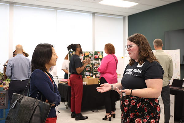 Katelyn France is talking with an event guest at the ETS Minnesota Business Accelerator finale. Other finalists and guests can be seen in the background.