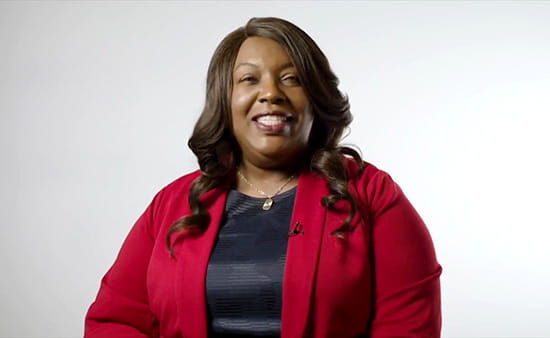 a video screen shot of a Black woman in a black top and red cardigan smiling