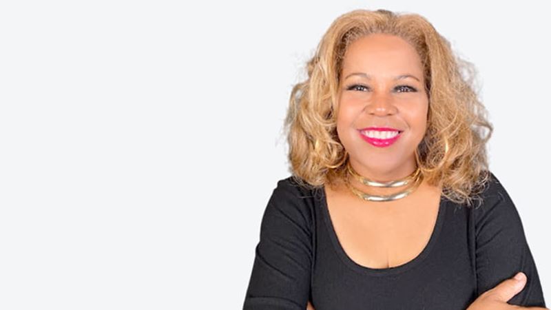 head shot of Sybil Wilkes, a Black woman smiling and wearing a black top and a silver necklace