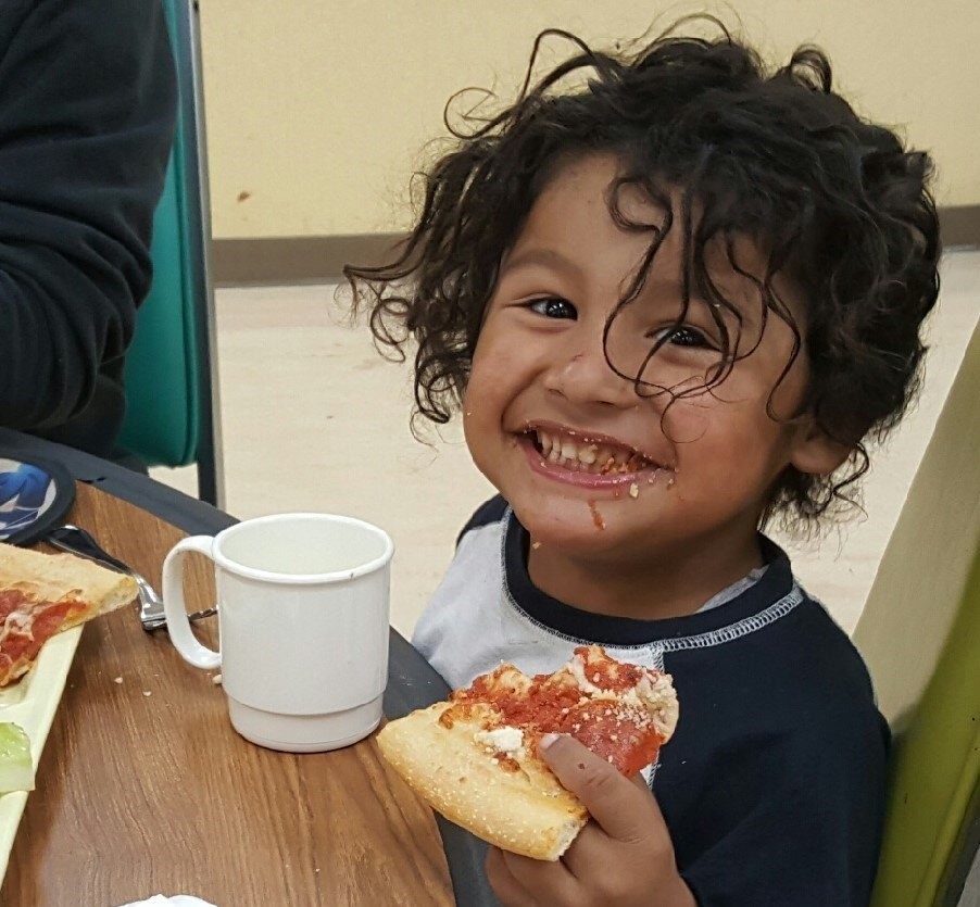 little kid eating pizza and smiling for camera