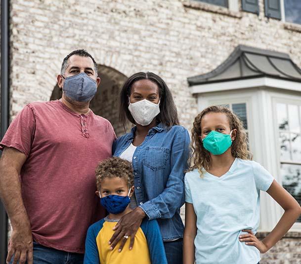 a diverse family wearing masks standing in front of a home