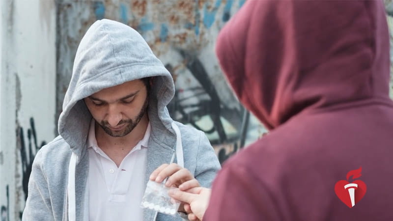 a Latino man in a grey hoodie purchasing pills on the street