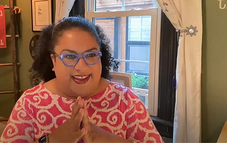 a still frame from the open mic night shows a woman in glasses actively participating in the event from inside her home