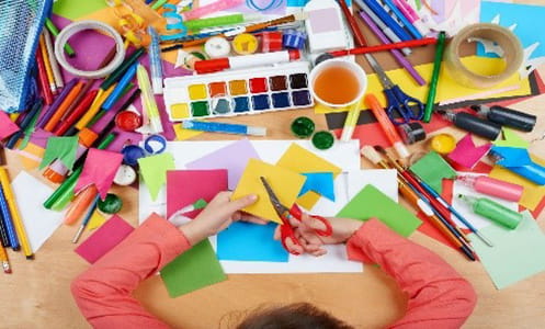 an aerial view of a person cutting paper over a table covered in art supplies