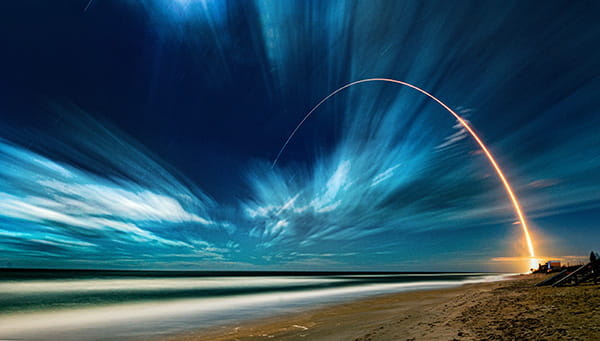 conceptual landscape of a beach and night sky with a gold streak arching over the ocean