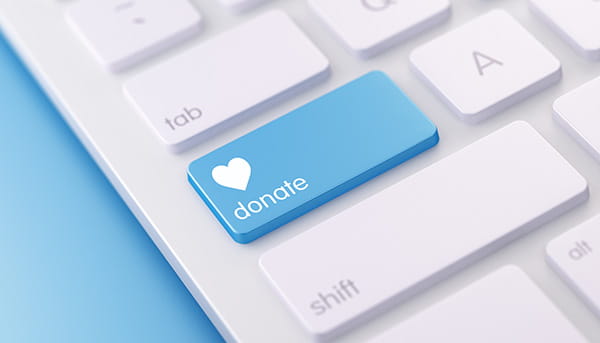 a cropped white computer keyboard with one blue key containing a white heart and the word donate
