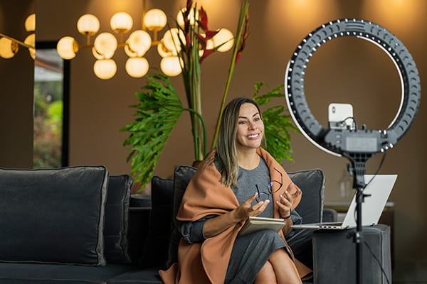 a professional Hispanic/Latina woman sitting on a sofa in front of her laptop and a ring light