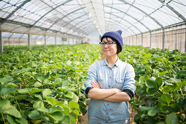 Asian woman standing with her arms crossed in a greenhouse with plants surrounding her