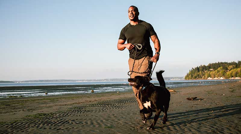 man running with pet dog on beach