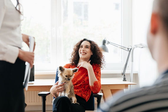 Women laughing and holding her dog in her lap while at work in a business meeting.
