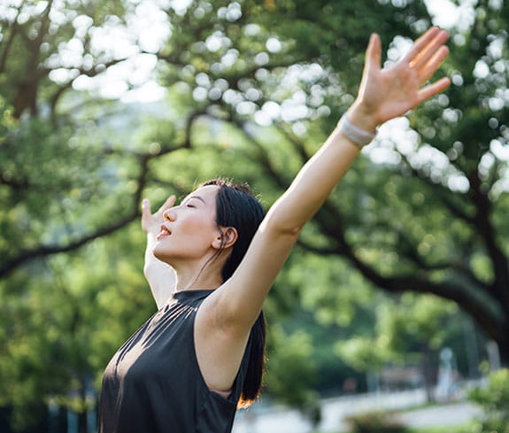 Young Asian sports woman with eyes closed stretching with arms outstretched.