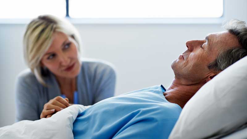 wife sitting by husband in hospital bed
