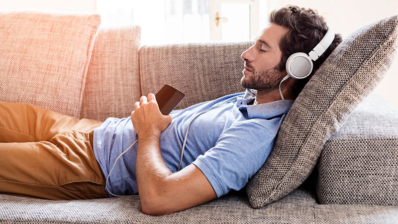 Man laying on couch listening with headphones
