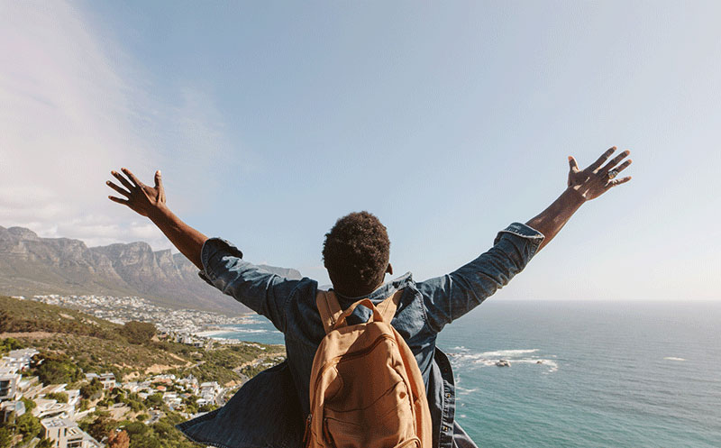 back of man with backpack raising arms in success