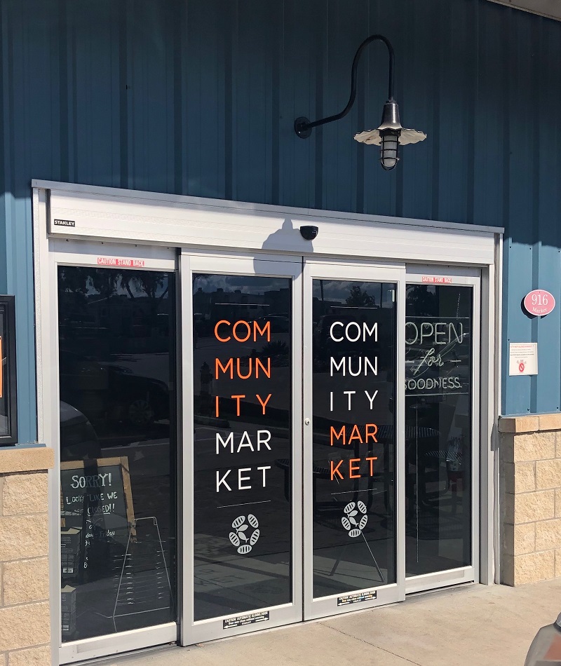 auto-open sliding glass doors on a storefront with decals spelling Community Market