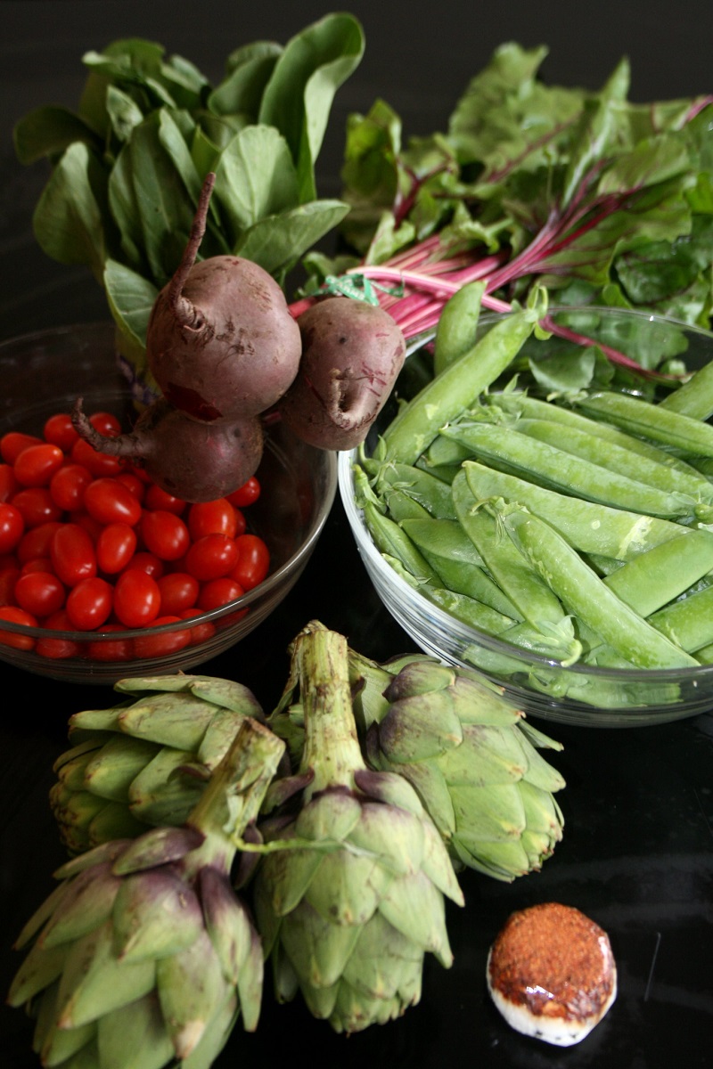 Fruits and vegetables in glass bowls and spread out on a surface.
