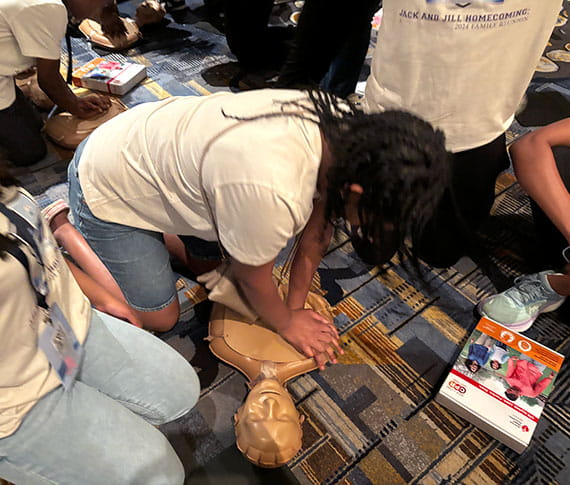 A group of teens from Jack and Jill of America, Inc., are giving chest compressions on a CPR practice manikin. A group of teens from Jack and Jill of America, Inc., are giving chest compressions on a CPR practice manikin.