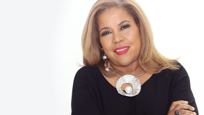 head shot of Sybil Wilkes, a Black woman with her arms crossed wearing a black top and a large silver statement necklace