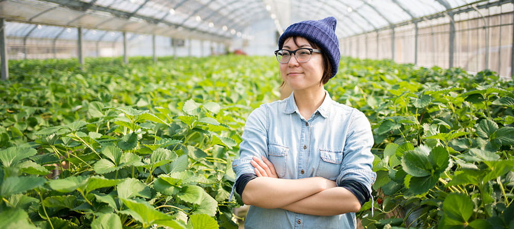 Asian woman standing with her arms crossed in a greenhouse with plants surrounding her Asian woman standing with her arms crossed in a greenhouse with plants surrounding her