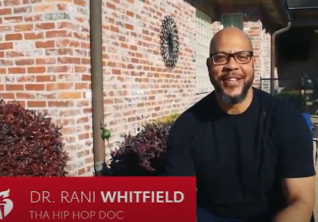 Dr. Rani Whitfield is standing outside a brick home and smiling. A red block with "Dr. Rani Whitfield, Tha Hop Hop Doc" in white letters is overlaying the image.