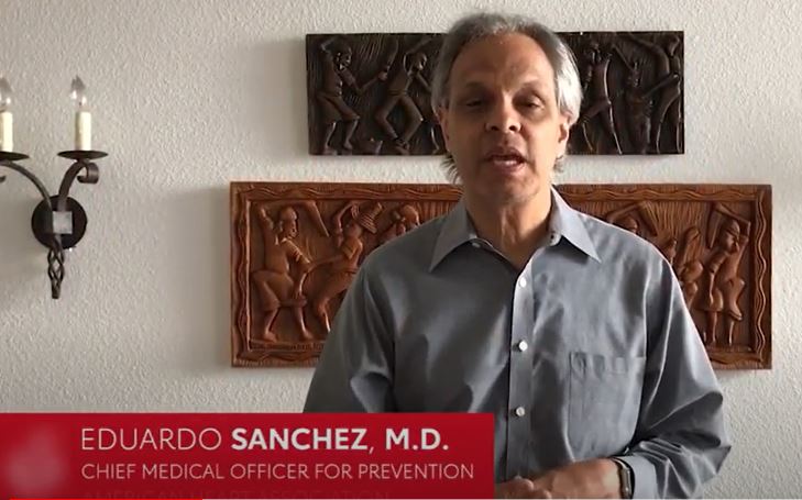 A video frame of Dr. Eduardo Sanchez in a room with wall art. A red block with "Eduardo Sanchez, M.D., Chief Medical Officer for Prevention" in white letters is overlaying the image.