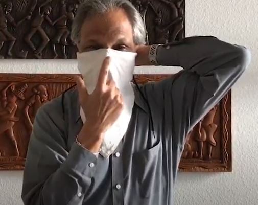 A video frame of Dr. Eduardo Sanchez in a room demonstrating using a white mask as a face covering.