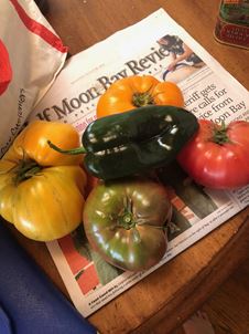 A pepper and a variety of large heirloom tomatoes are sitting on top of the Half Moon Bay Review newspaper. A pepper and a variety of large heirloom tomatoes are sitting on top of the Half Moon Bay Review newspaper.